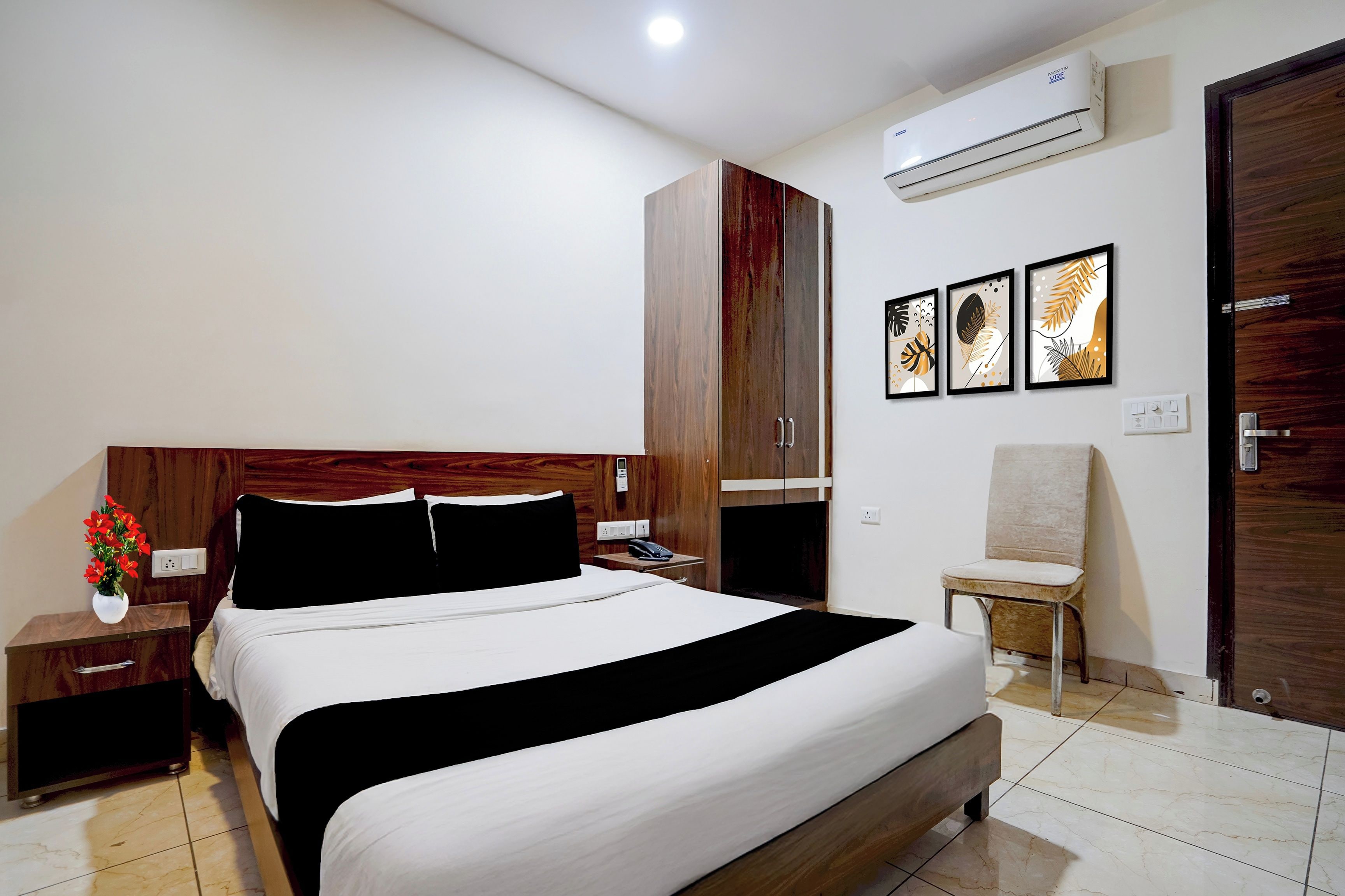 Une chambre d’hôtel comprenant un lit, des tables de chevet, une petite table, une chaise, un appareil de climatisation et des œuvres d’art accrochées au mur.
