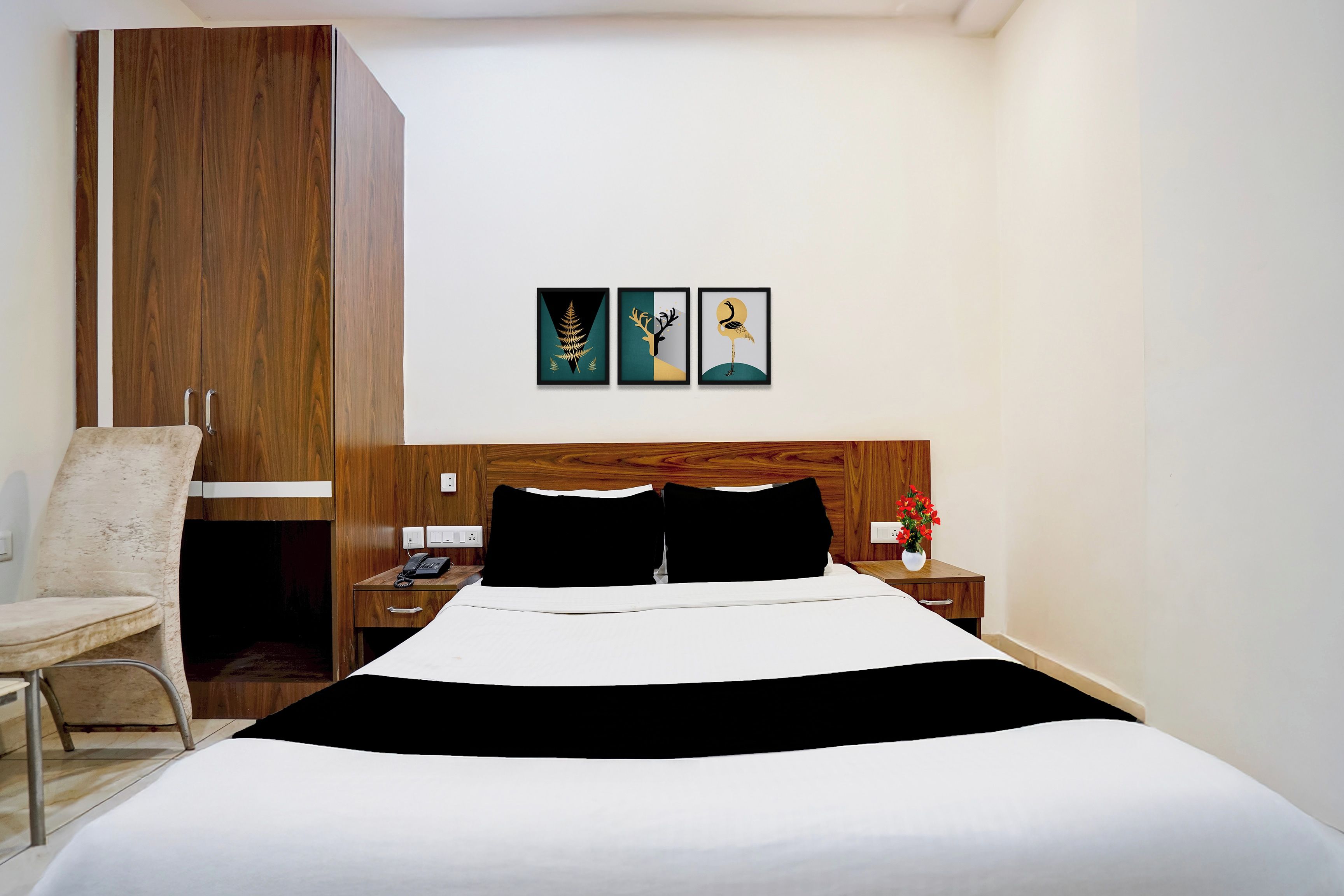 Une chambre d’hôtel avec un grand lit, une armoire en bois, un bureau avec un téléphone et une chaise. Trois tableaux encadrés sont accrochés au mur.