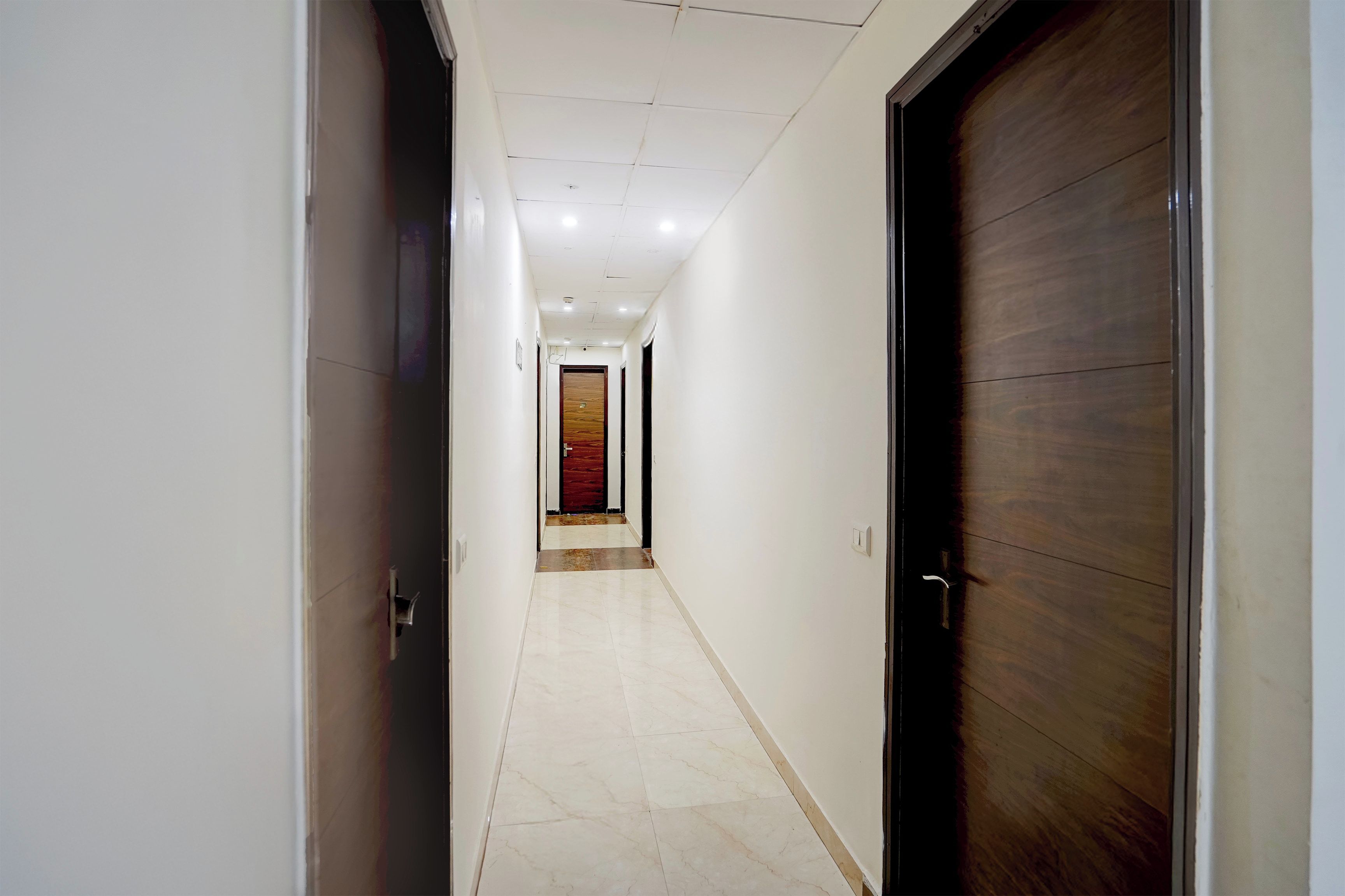 A corridor with a tiled floor, a wooden door on the right, and a red carpet leading to a room.