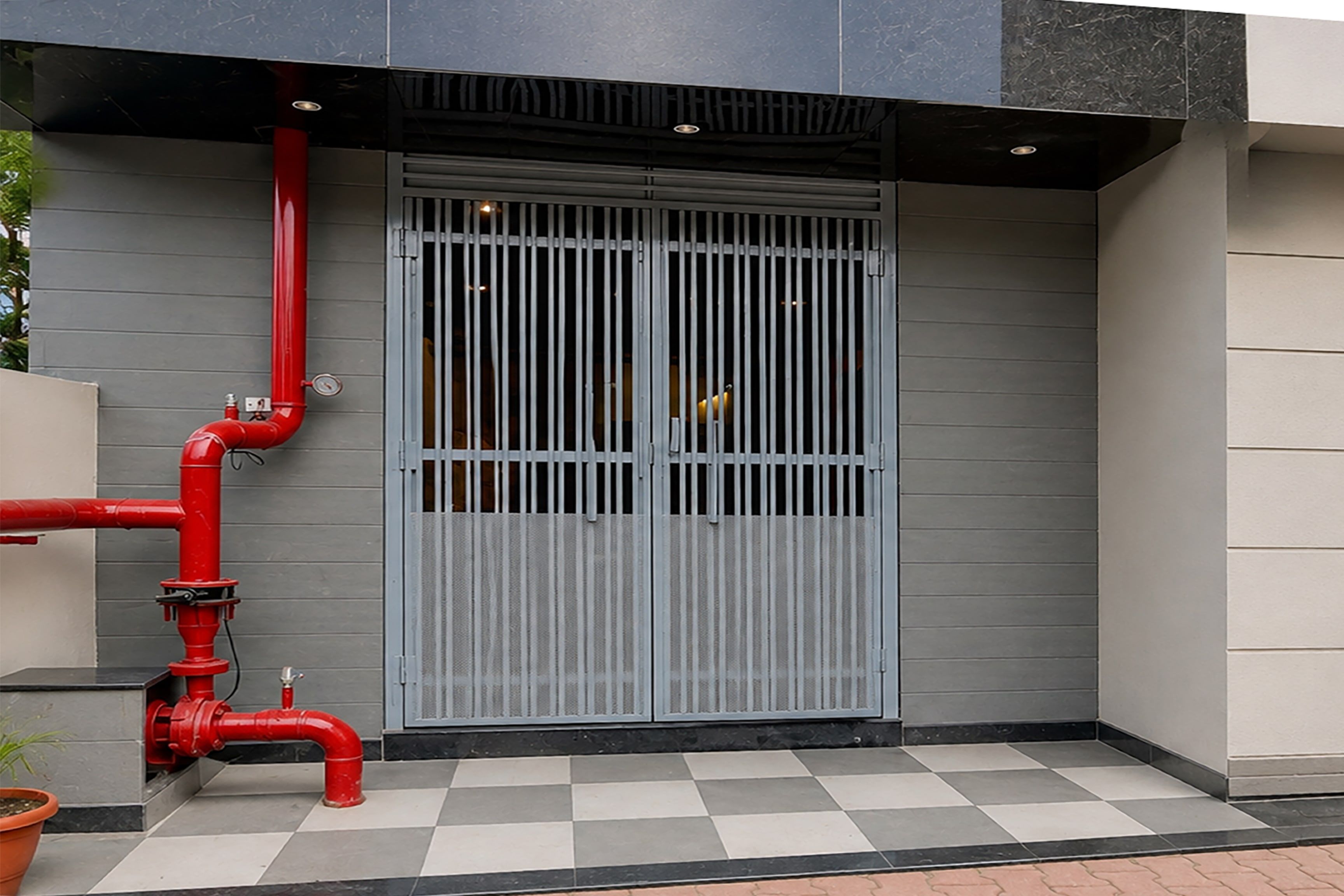 A building entrance with a grey metal gate, red pipes, and a checkered floor.
