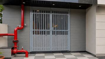 A building entrance with a grey metal gate, red pipes, and a checkered floor.