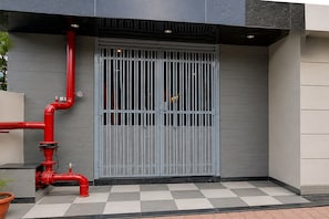 Una entrada de edificio con una verja metálica gris, tuberías rojas y un suelo a cuadros.