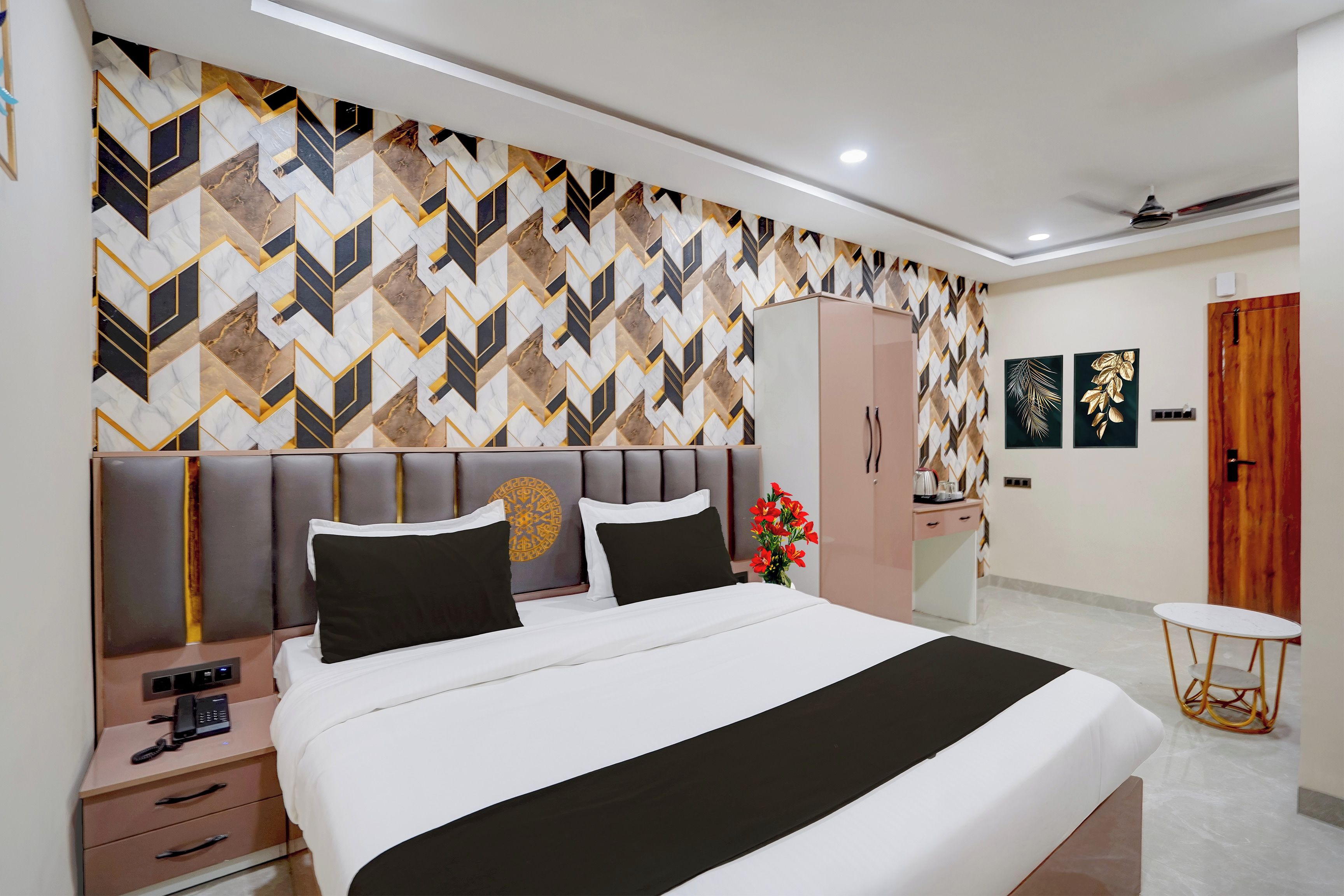 A hotel room with a bed, bedside table, nightstand, wardrobe, and a small round table with a chair.