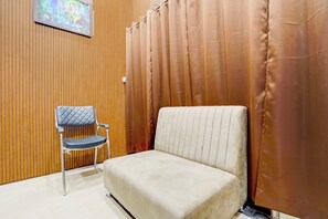 Una habitación con una silla acolchada, un panel de pared de madera y una cortina.