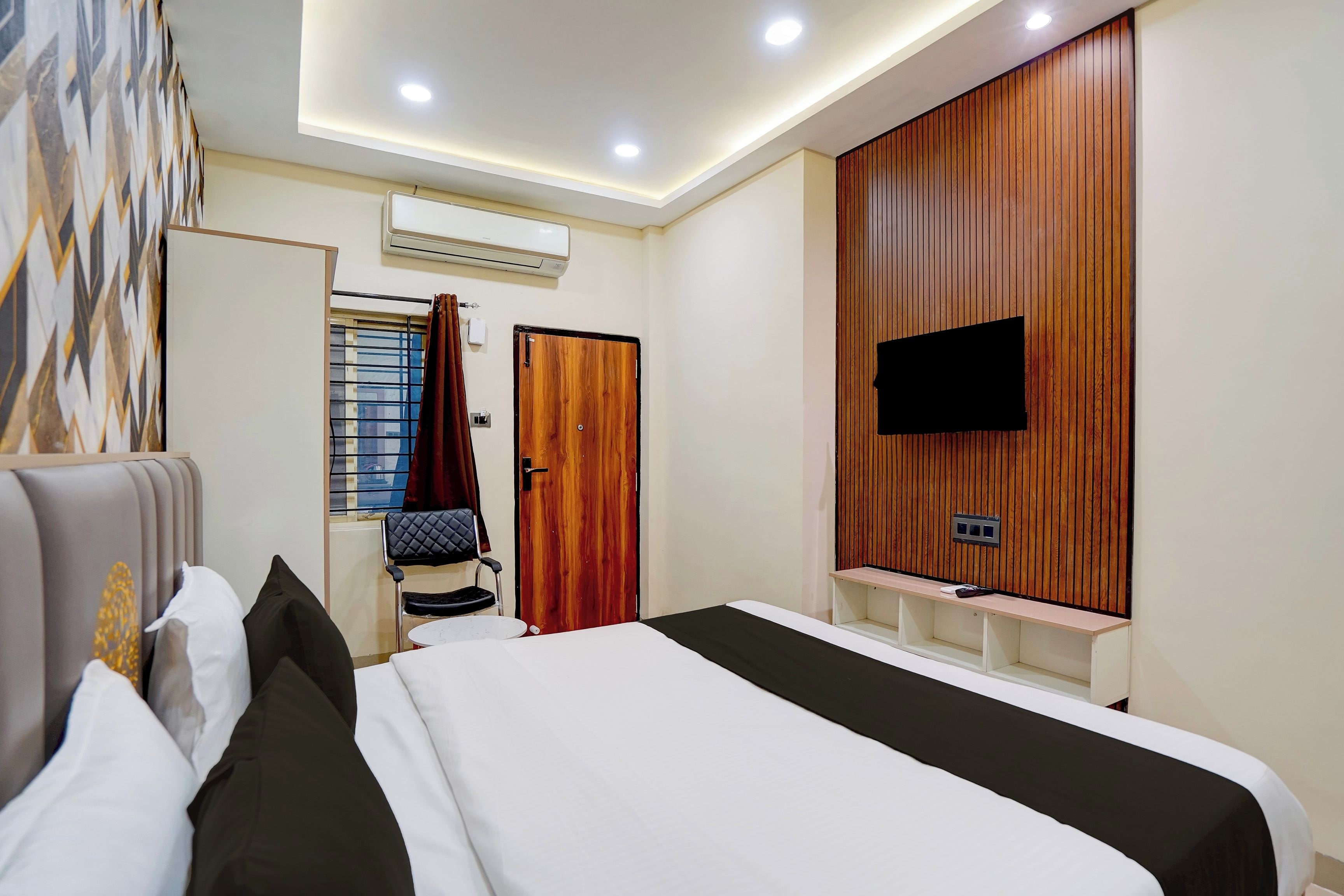 A hotel room with a bed, a TV mounted on the wall, a wardrobe, and an air conditioning unit.