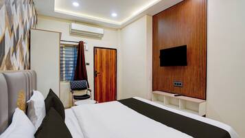 A hotel room with a bed, a TV mounted on the wall, a wardrobe, and an air conditioning unit.