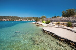 A coastal area with clear blue water, a stone wall, and a small green tent. - A3 - Modern apartment with garden and balcony with sea view, 80m from beach (Vinišće)