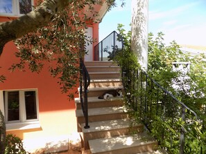A staircase with a cat lying on the steps, surrounded by greenery and a building with a red facade. - A3 - Modern apartment with garden and balcony with sea view, 80m from beach (Vinišće)