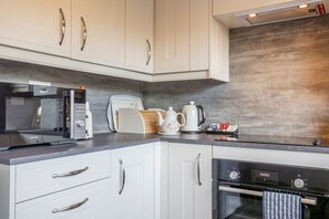 A modern kitchen with white cabinetry, a microwave, a coffee maker, and a kettle. - Warrack Street (No 37) | St Andrews (St Andrews)
