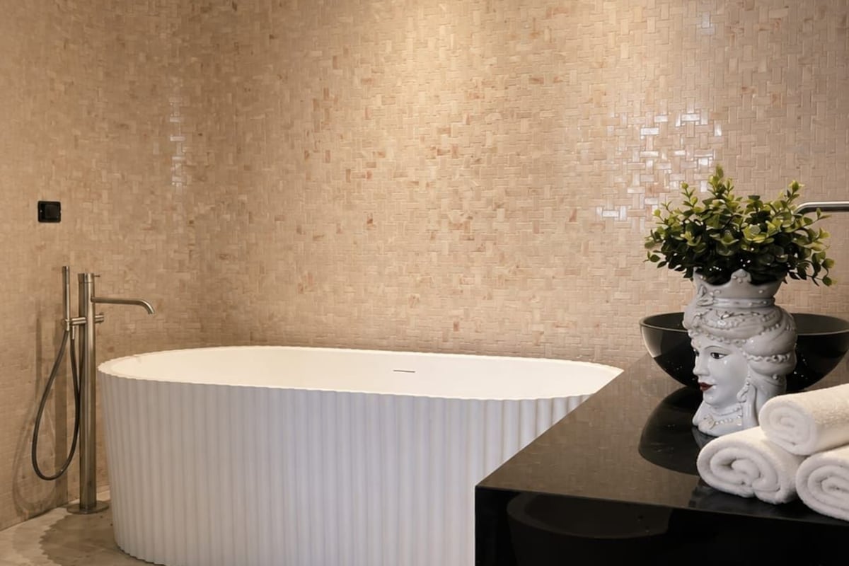 Un baño moderno con una bañera independiente, un tocador negro y una planta en maceta.