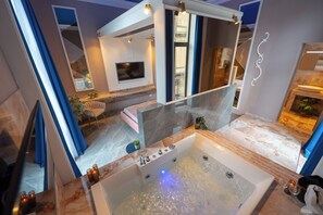 Un bagno moderno con una grande vasca, una TV e un angolo relax con una pianta.