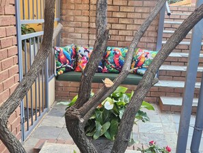 Una escalera con un banco decorado con coloridos cojines de aves del paraíso, una reja de metal y una pared de ladrillo.