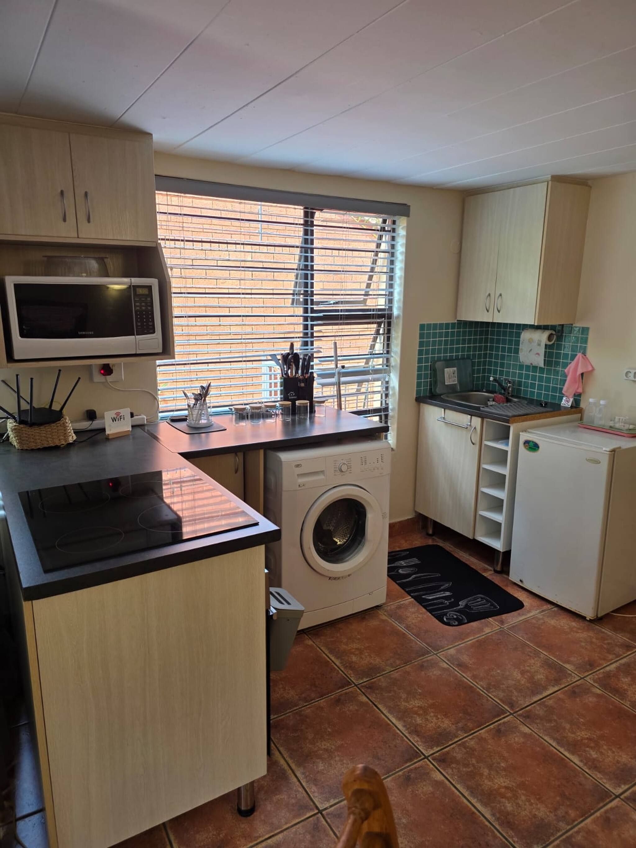 A compact kitchen with a microwave, washing machine, sink, and a small refrigerator.