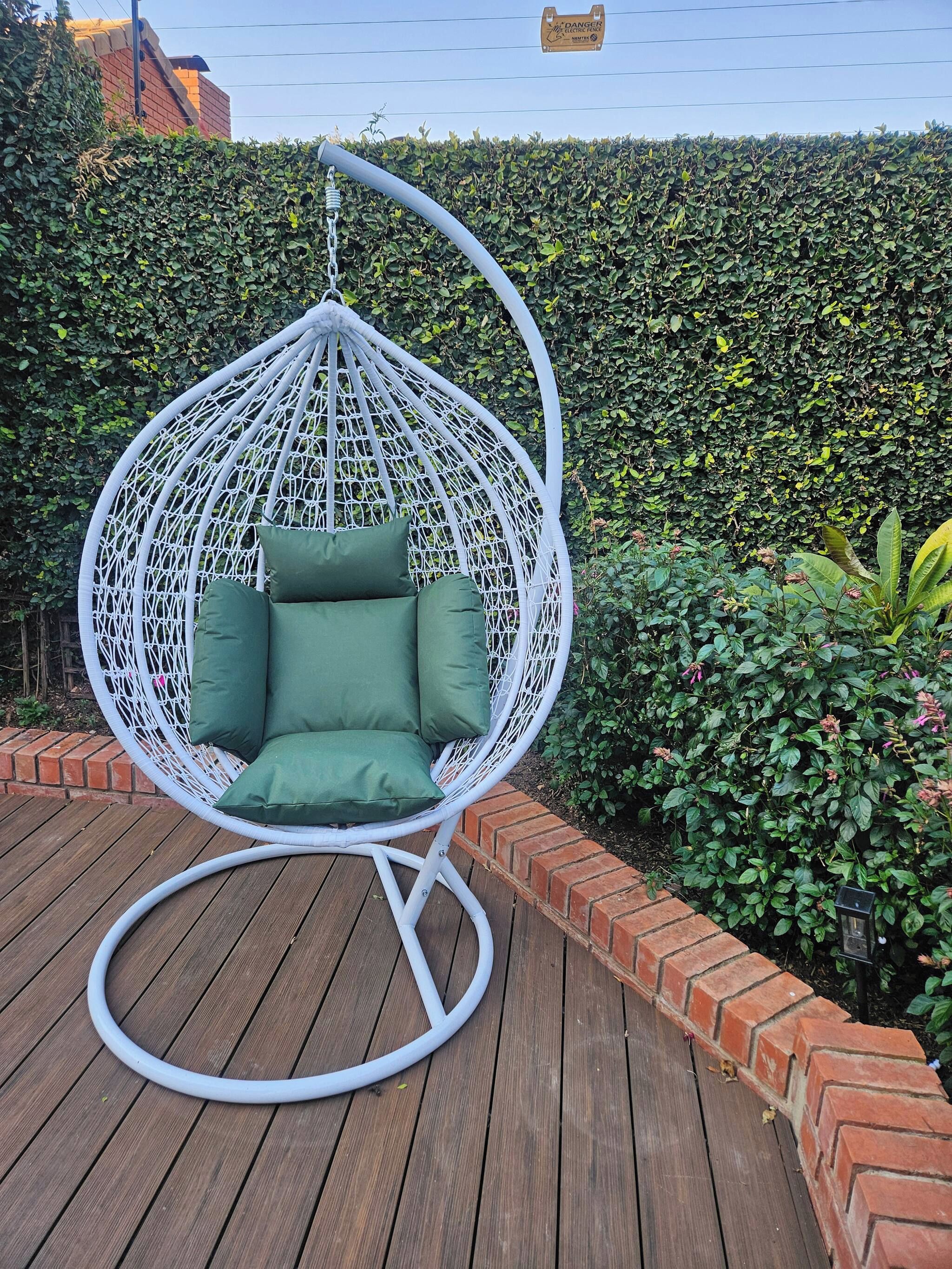 A white hanging chair with green cushions on a wooden deck.