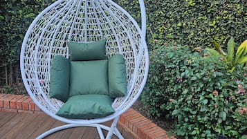 A white hanging chair with green cushions on a wooden deck.