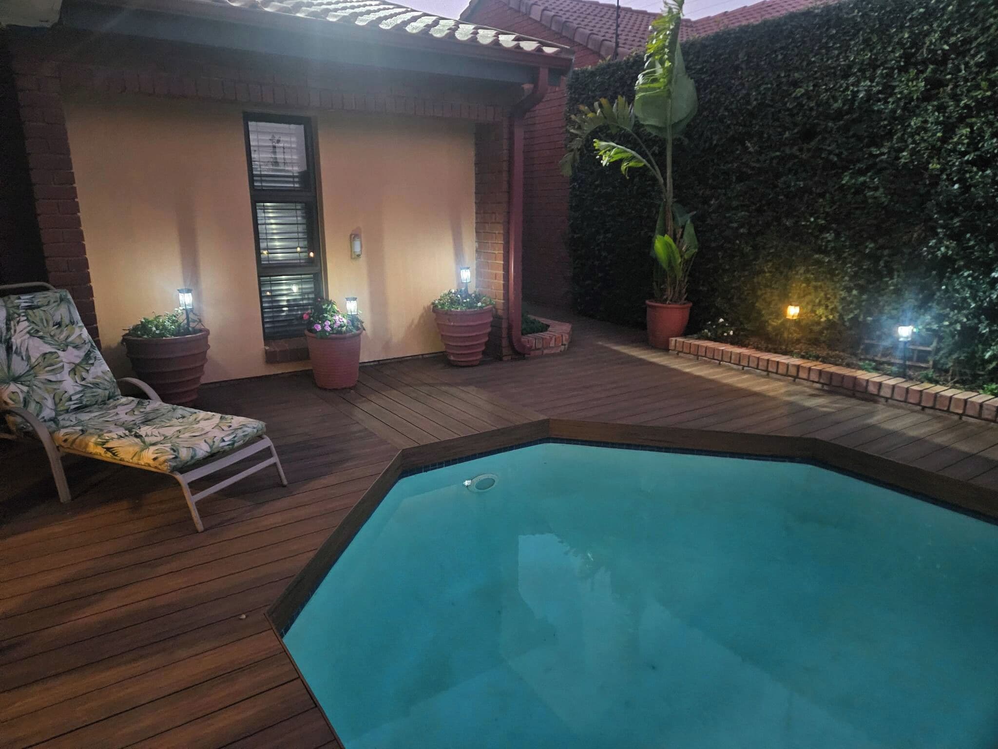 Un área de piscina con terraza de madera, una silla de descanso y plantas en macetas.