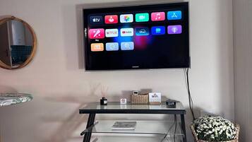 A flat-screen TV mounted on a wall with a glass stand below it, a Wi-Fi sign, and a decorative basket on the floor.
