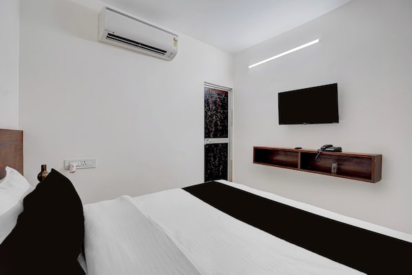 A hotel room with a bed, a flat-screen TV mounted on the wall, an air conditioning unit above the bed, a bedside table with a phone, and a wall socket. - Hotel O Ayodhya Junction Road (Faizabad)