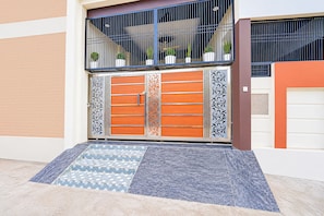 A gated entrance with a patterned tile entrance mat, a metal gate with decorative panels, and potted plants on the balcony. - Hotel O Ayodhya Junction Road (Faizabad)