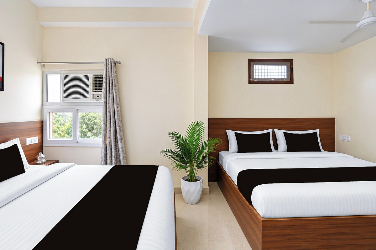 A hotel room with two beds, a window with curtains, an air conditioning unit, a small window, and a ceiling fan.