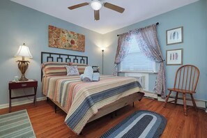 A bedroom with a bed, a nightstand, a lamp, a ceiling fan, a window with curtains, and a chair. - Graceful Stays: Highlands 1BR near Dining – Unit 11 (Louisville)