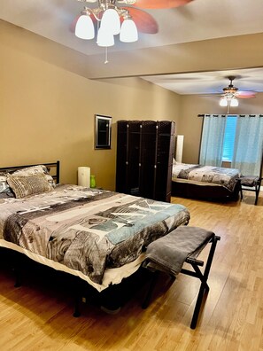 A bedroom with a large bed, a smaller bed, a bench, a wardrobe, a ceiling fan, and a window with curtains. - Peaceful Laurel Lake Retreat with Private Waterfall Trail (Corbin)