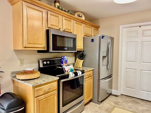 A kitchen with wooden cabinets, a microwave, a stove, a refrigerator, and a trash bin. - Peaceful Laurel Lake Retreat with Private Waterfall Trail (Corbin)