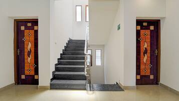 Una escalera conduce a un piso superior, flanqueada por dos puertas con paneles decorativos y números.