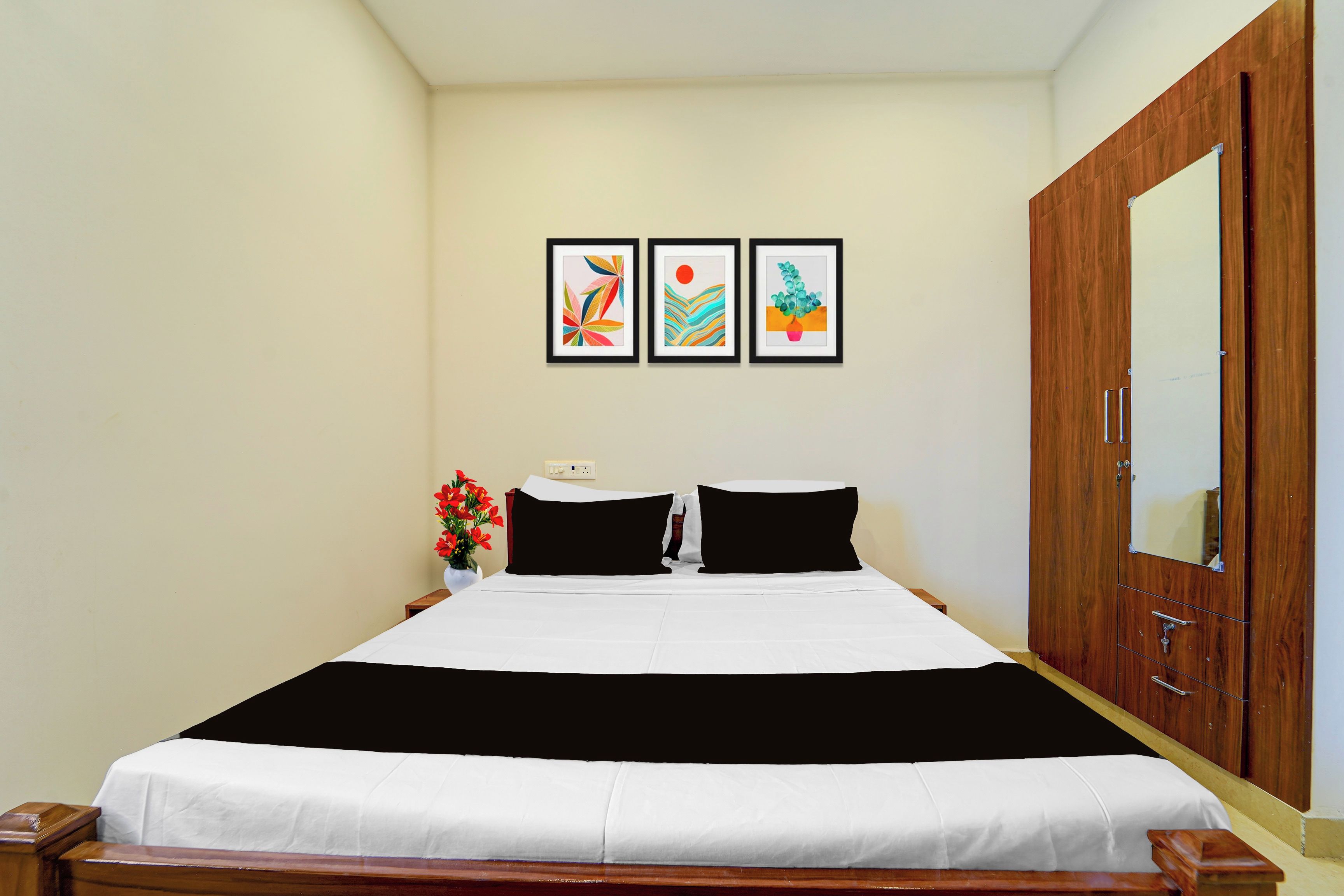 Habitación de hotel con cama, armario, mesita de noche con un jarrón de flores y tres cuadros enmarcados en la pared.