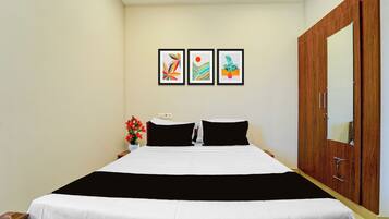 Habitación de hotel con cama, armario, mesita de noche con un jarrón de flores y tres cuadros enmarcados en la pared.