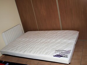 Ein Einzelzimmer mit einem weißen Bett, einem Holzschrank und einer Heizung.