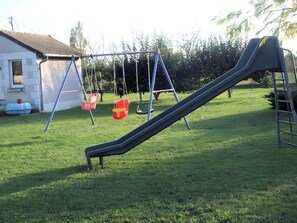 Ein Spielplatz mit Rutsche und Schaukeln in einem grünen Rasen.