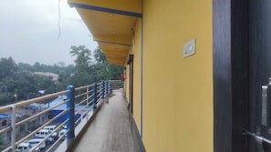 A balcony with a yellow wall, a metal railing, and a view of parked cars and buildings in the background.