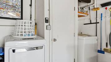 A laundry area with a washing machine, a drying rack, and various cleaning tools.