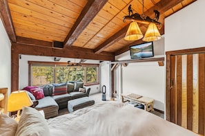 Une chambre à coucher avec un grand lit, un canapé, une télévision et une fenêtre donnant sur la forêt.