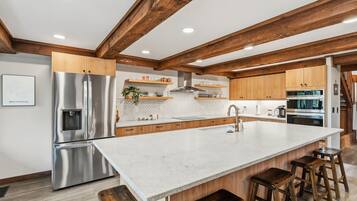 Een moderne keuken met een groot eiland, roestvrijstalen apparatuur, houten balken en een backsplash van visgraatmozaïektegels.