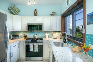 A kitchen with white cabinets, a stainless steel refrigerator, a stove, and a microwave. - Lavender Hill - Mermaid’s Tale #10E – Renovated 1-Bedroom Condo with Cruz Bay Harbor Views (St John)