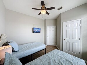 Ein Schlafzimmer mit zwei Betten, einem Deckenventilator, einer Tür und einem Wandbild.