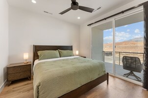 Un dormitorio con cama, mesita de noche, lámpara y vistas a un balcón con una silla.