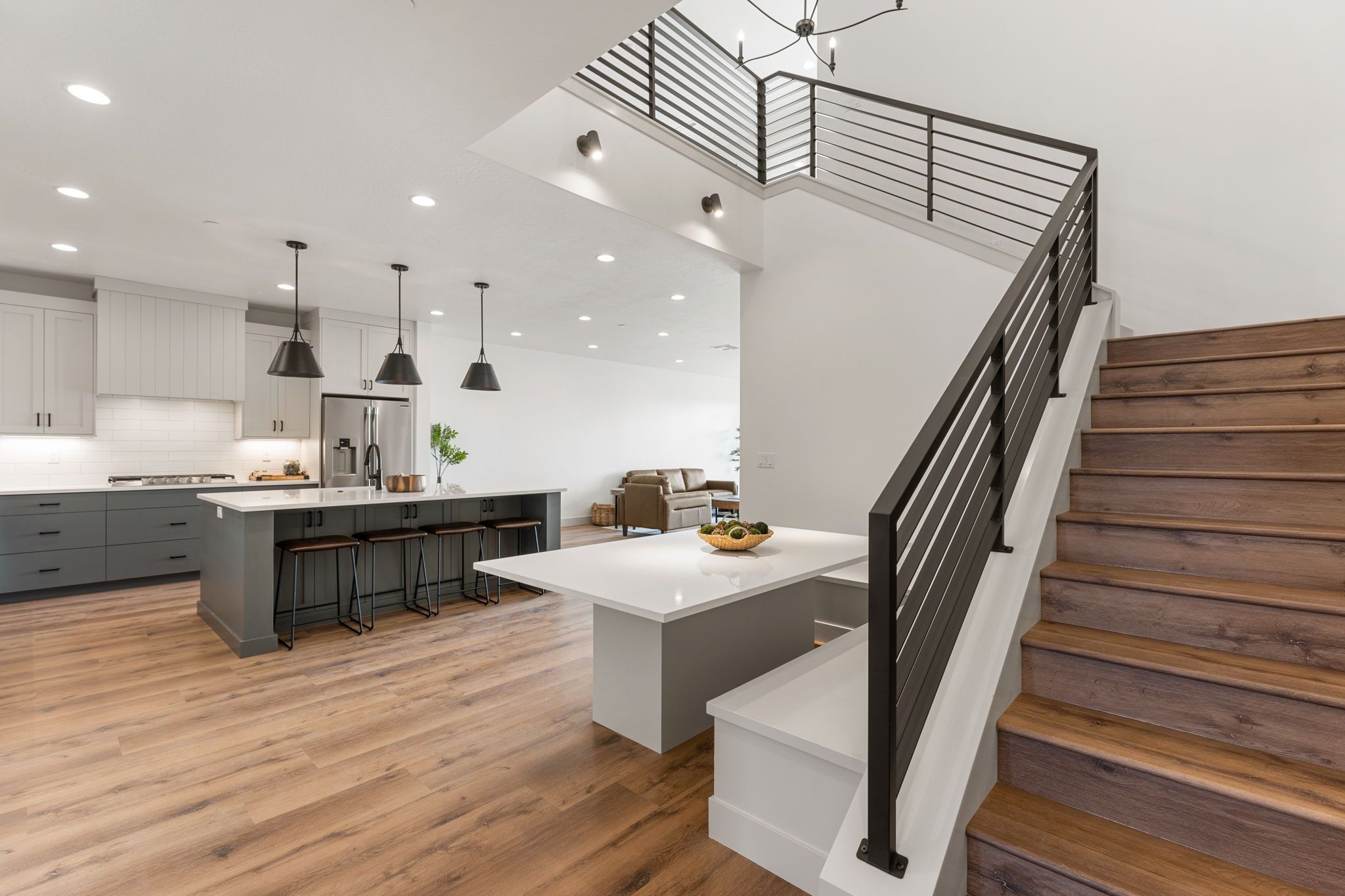 A modern kitchen with a central island, bar stools, and a staircase with wooden steps.