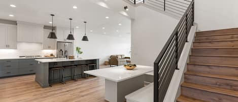 A modern kitchen with a central island, bar stools, and a staircase with wooden steps.