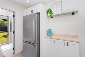 A modern kitchen with a stainless steel refrigerator, white cabinetry, and a small plant on a shelf. - Big Island Kahaluu Surf Boutique #2 2 Bedroom Apts (Kailua-Kona)