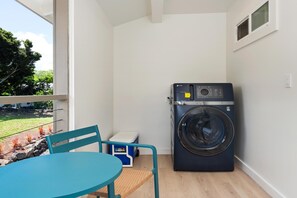 A compact room with a washing machine, a small table, and a chair. - Big Island Kahaluu Surf Boutique #1 2 Bedroom Apts (Kailua-Kona)