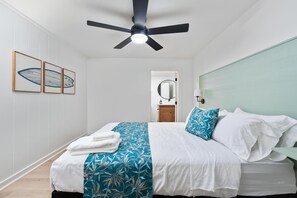 A bedroom with a bed, a ceiling fan, a nightstand, a mirror, and a door leading to another room. - Big Island Kahaluu Surf Boutique #1 2 Bedroom Apts (Kailua-Kona)
