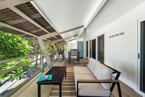 En balkon med en sofa, et bord og en stol, med udsigt over en have med forskellige planter og et udendørs vue.