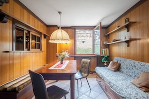 A room with wooden paneling, a dining table with chairs, a sofa, a window with a view, and a hanging lamp. - Three-room apartment in Giomein, private garage, right on the slopes (Breuil-Cervinia)