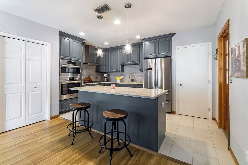 A modern kitchen with grey cabinets, stainless steel appliances, a central island with stools, and pendant lighting.