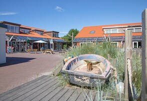 Une propriété située au bord de l’eau, comprenant un bateau, une terrasse en bois et des bâtiments dont les toits sont recouverts de tuiles rouges.