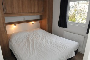 A small, single-bed room with a wooden headboard, a window with a view of trees, and a radiator. - Lovely Villetta on the Wadden Island of Texel (Den Burg)