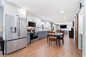 A modern kitchen with white cabinetry, stainless steel appliances, and a dining area with wooden chairs. - Room for ten in the heart of Bayfield village (Bayfield)